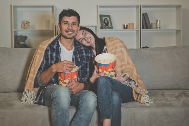 O casal feliz comendo pipoca e assistindo filme no sofá