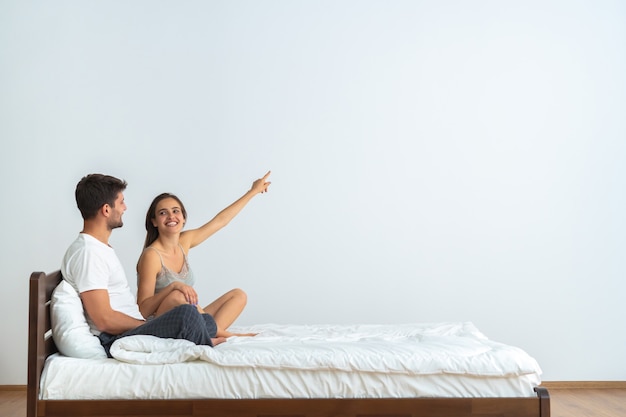 Foto o casal feliz na cama gesticulando no fundo branco