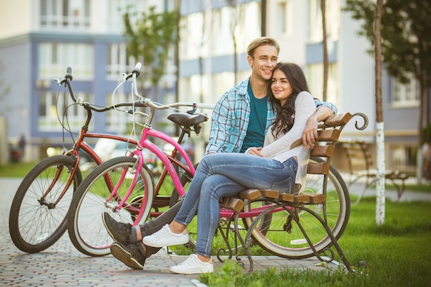 O casal feliz senta no banco perto de bicicletas