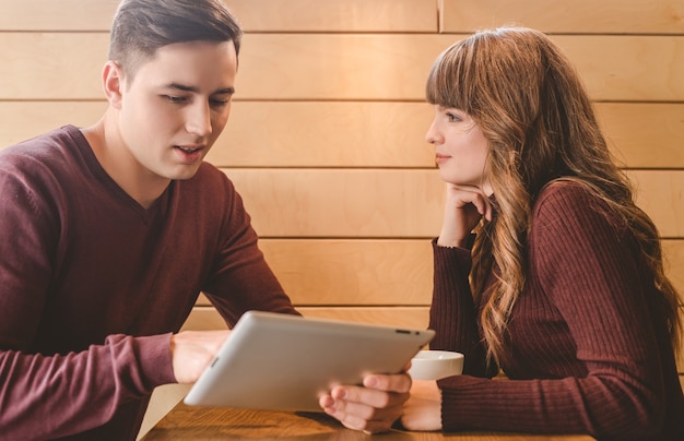 O casal feliz sentado com um tablet na mesa do restaurante