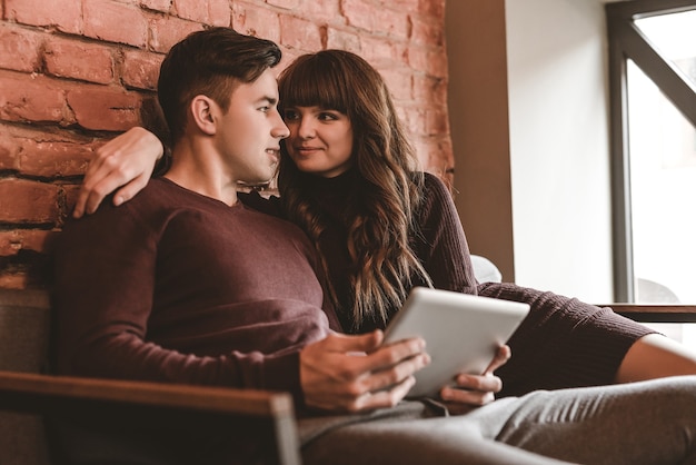 O casal feliz sentado com um tablet no restaurante