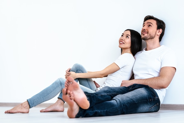 O casal feliz sentado no fundo da parede branca