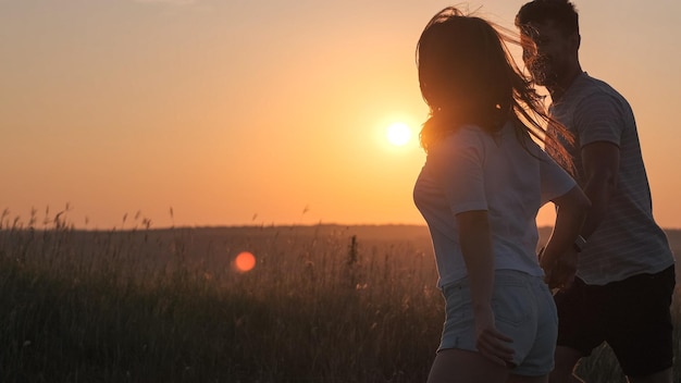 O casal romântico jogando no topo da montanha no fundo do pôr do sol