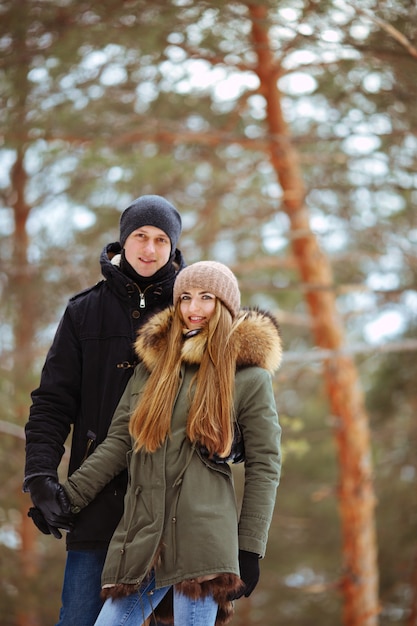 O casal se abraça em um bosque nevado contra um fundo de árvores