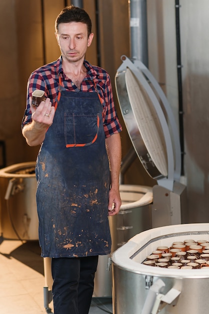O ceramista masculino caucasiano de meia idade no avental inspeciona a qualidade de panelas de barro após queima no forno na oficina de cerâmica.
