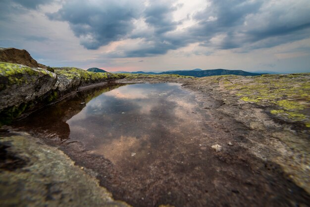 O céu azul refletiu no lago pequeno no pico de montanha rochosa na cordilheira azul no alvorecer.