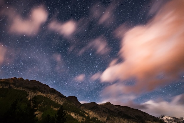 O céu estrelado com nuvens de movimento borrado e luar brilhante. Alpes europeus