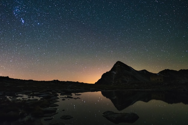 O céu estrelado de astro refletiu no lago na alta altitude nos cumes. constelação de orion a brilhar.