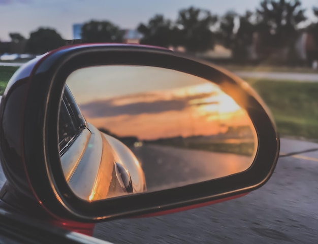 Foto o céu refletindo-se no espelho lateral do carro durante o pôr-do-sol