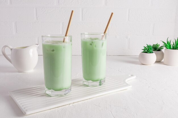 O chá matcha latte mais útil em dois copos contra uma parede de tijolos brancos e plantas em vasos de flores Detox luta contra o envelhecimento da pele