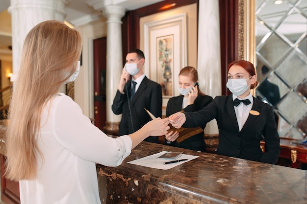 O check-in do hotel. recepcionista no balcão do hotel usando máscaras médicas como precaução contra vírus. Mulher jovem em viagem de negócios fazendo check-in no hotel