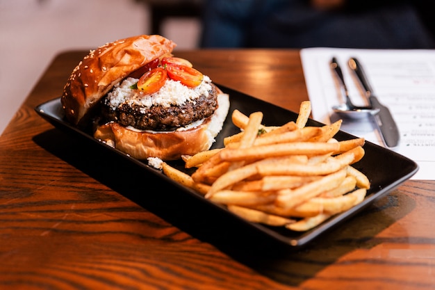 O cheeseburger com carne grelhada, queijo de feta e tomate cortado serviu com fritadas na placa preta.