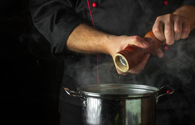 O chef adiciona pimenta moída a uma panela de comida fervente Conceito de culinária de cozinha Retsoran com espaço publicitário em fundo preto