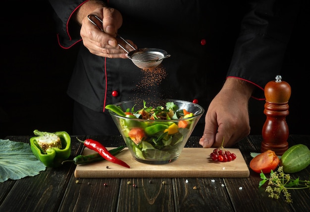 O chef adiciona sabor à salada de legumes Comida vegetariana pelas mãos do cozinheiro na cozinha Ideia de menu para um hotel ou restaurante