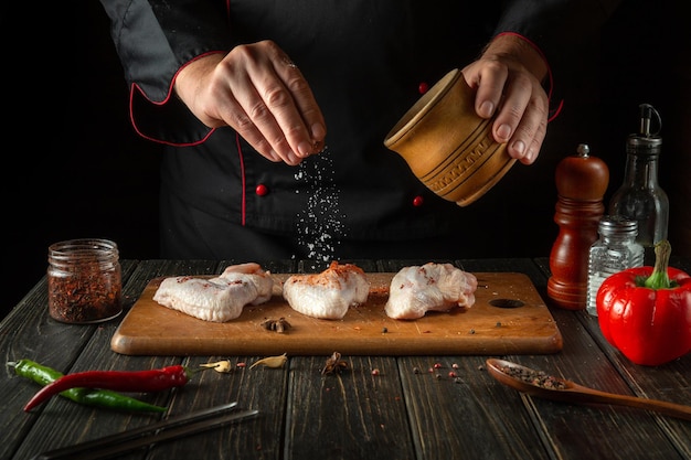 O chef adiciona sal às asas de frango cruas Cozinhando pepitas de frango na cozinha de um restaurante