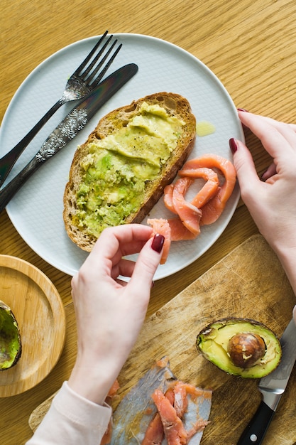 O chef coloca o salmão na torrada com avacado em uma torrada de pão preto.