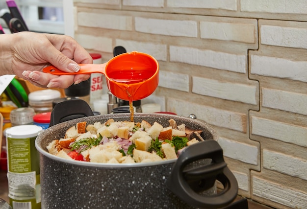 O chef coloca óleo na caçarola do fogão a gás com legumes para a sopa e pedaços de baguete