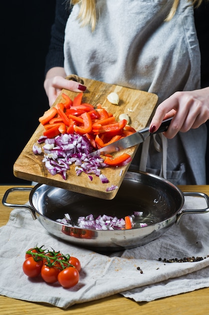 O chef coloca pimentões e cebolas vermelhas picadas com uma faca na panela.