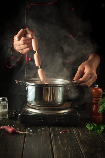 O chef coloca salsichas em uma panela fervendo cozinhando delicioso café da manhã ou jantar na cozinha