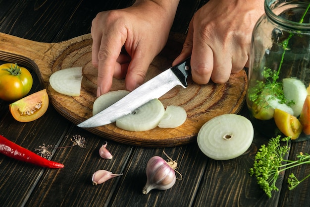 Foto o chef corta a cebola com uma faca em uma tábua de cozinha para preservação em uma jarra deliciosos vegetais enlatados pelas mãos do cozinheiro