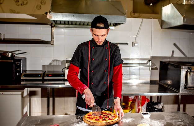 O chef corta a pizza com uma faca para servir