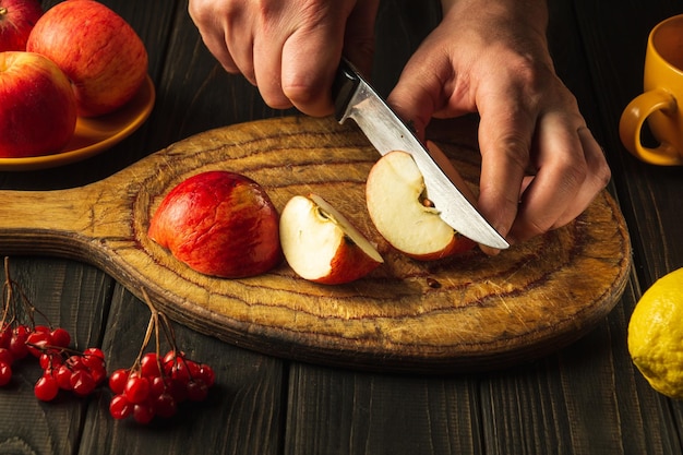 O chef corta maçãs em uma tábua com uma faca para fazer compota ou suco de frutas