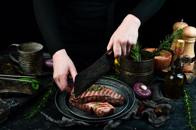 O chef corta o bife grelhado em um fundo de pedra preta