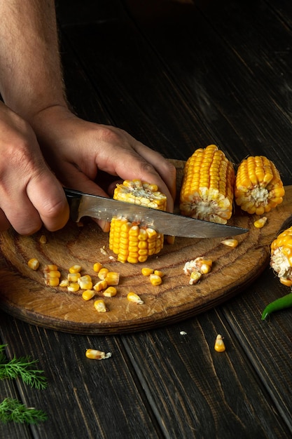 O chef corta o milho com uma faca O milho é um excelente café da manhã ou almoço dietético preparado pelas mãos do cozinheiro