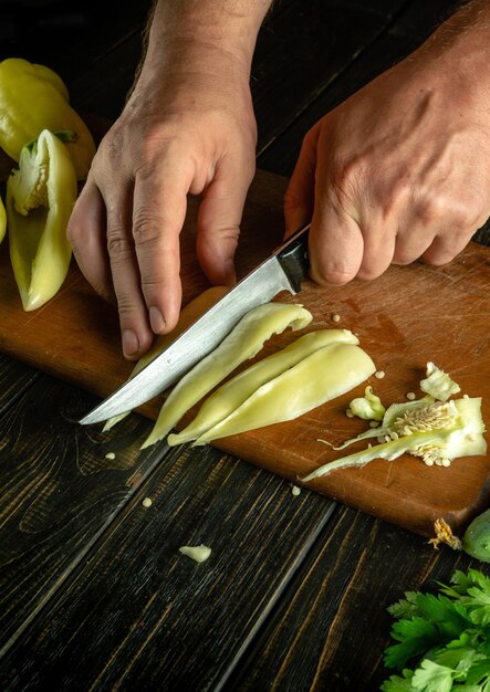 O chef corta pimentas frescas amarelas em uma tábua de cortar para preparar um delicioso lecho em casa A ideia de cozinhar uma dieta de vegetais na mesa da cozinha