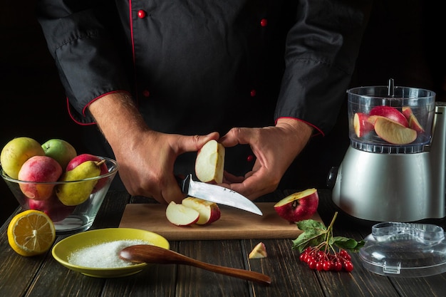 O chef corta uma maçã para preparar uma bebida doce de frutas em um liquidificador ou mixer Menu ou ideia de receita para um café da manhã ou jantar vegetariano saudável