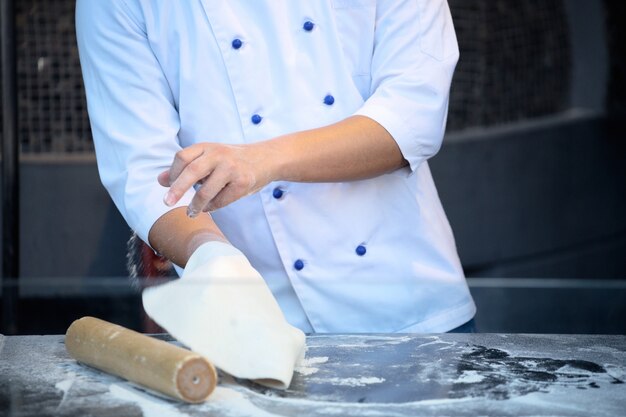 O chef de avental preto faz massa de pizza com as mãos sobre a mesa.