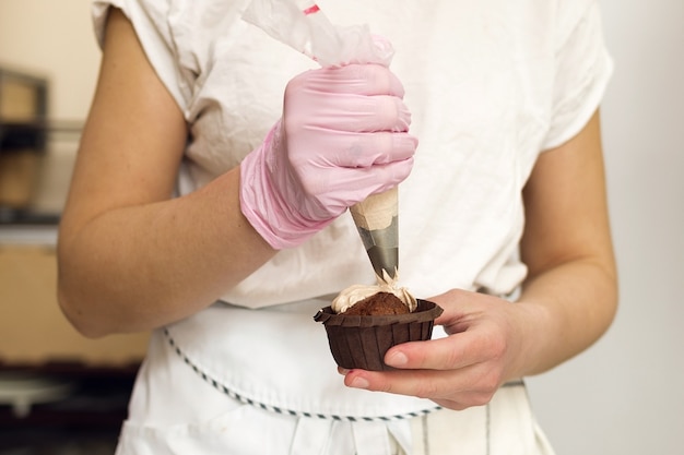 O chef de confeitaria aplica creme no muffin de chocolate