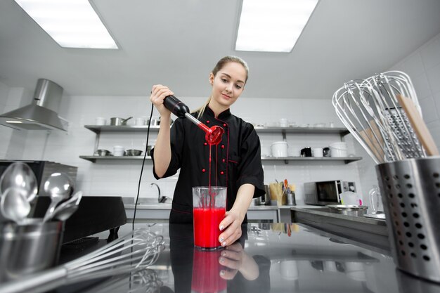 O chef de confeitaria prepara a cobertura vermelha do bolo para o bolo com um liquidificador.