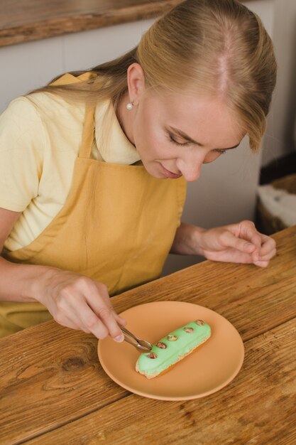 O chef de pastelaria de mulher bonita decora o éclair. Conceito de cursos de confeitaria ou culinária