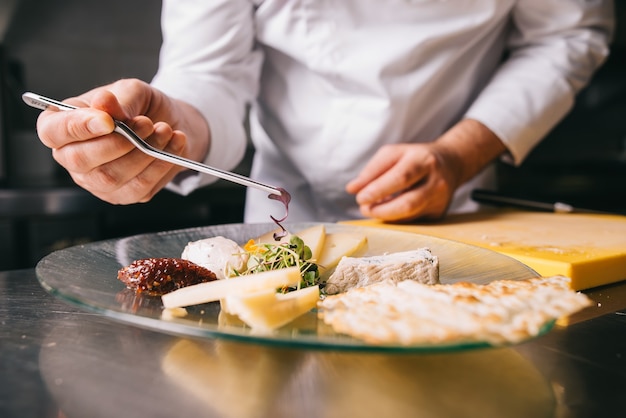 O chef decora um prato de queijo com uma pinça