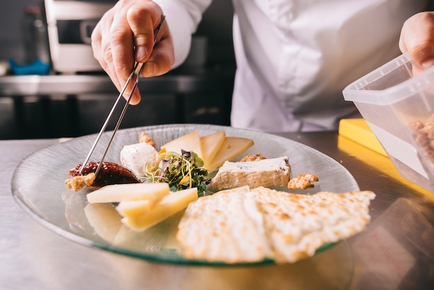 O chef decora um prato de queijo com uma pinça