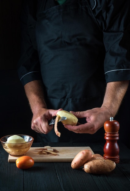 O chef descasca batatas para batatas fritas Para pratos de batata No conceito de fundo preto para menu