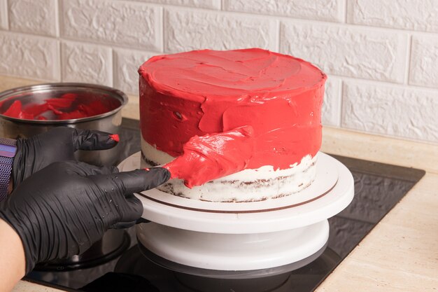 O chef enluvado cobre o bolo com creme vermelho usando uma espátula