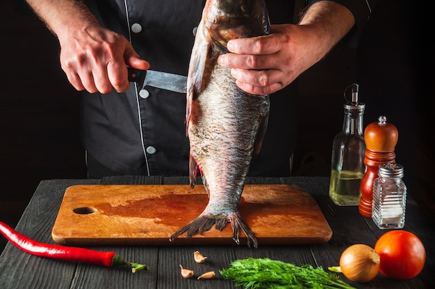 O chef está limpando uma carpa cabeça-gigante. ambiente de trabalho na cozinha do restaurante. conceito de dieta de peixes