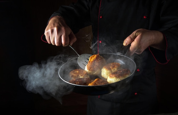 O chef está preparando oladki em uma frigideira O conceito de preparar prato nacional ucraniano ou bliny na cozinha Espaço preto para receita ou menu