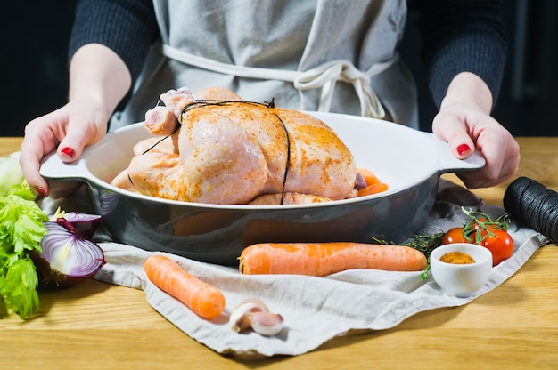 O chef está segurando uma panela com frango marinado inteiro.