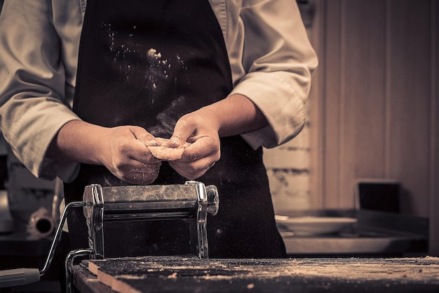 O chef faz massa para macarrão em uma mesa de madeira