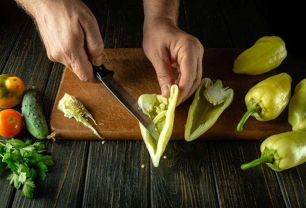 O chef limpa pimentões frescos amarelos em uma tábua com uma faca para preparar um delicioso prato de vegetais O conceito de cozinhar dieta vegetal na mesa da cozinha