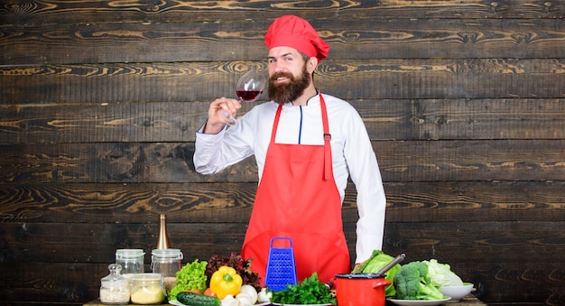 O chef mestre do homem segura o copo de vinho Qual vinho serve no jantar Conceito de jantar requintado Degustação de vinhos Como combinar vinho e comida como especialista Hipster usar chapéu e avental desfrutar do aroma da bebida