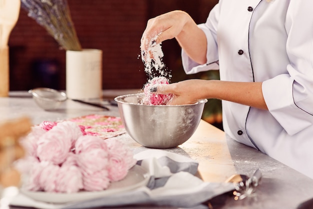 Foto o chef polvilha marshmallows caseiros com açúcar em pó. o conceito de cozinha caseira. processo de preparação de marshmallow.