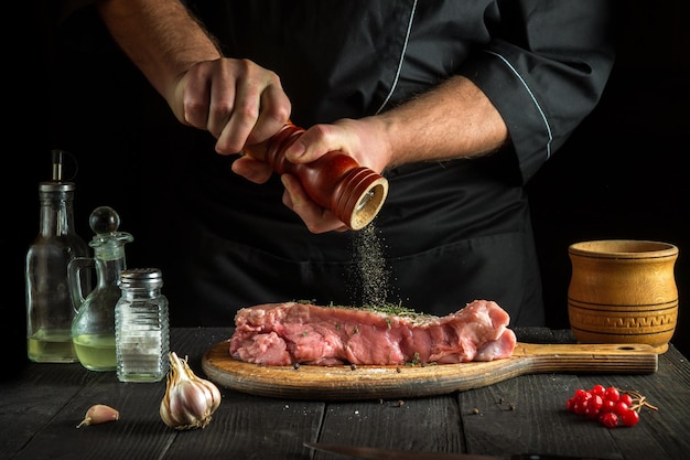 O chef prepara carne de vitela crua antes de assar, o chef adiciona pimenta à carne