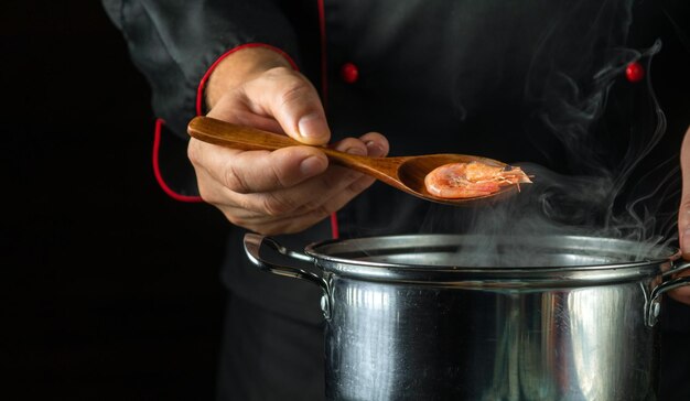 O chef prepara deliciosos camarões em uma panela na cozinha o conceito de um delicioso almoço de camarão para um restaurante colher na mão do cozinheiro wis camarão