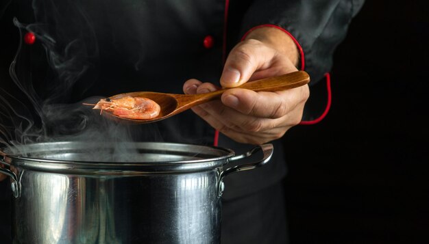 O chef prepara deliciosos camarões em uma panela na cozinha o conceito de um delicioso almoço de camarão para um restaurante colher na mão do cozinheiro wis camarão