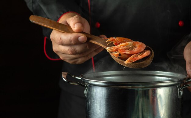 O chef prepara deliciosos camarões em uma panela na cozinha O conceito de um delicioso almoço de camarões para um hotel Colher na mão do cozinheiro wis scampi