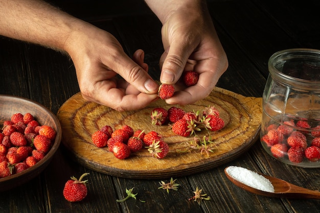 O chef prepara uma bebida de frutas doces de morangos frescos e açúcar na mesa da cozinha O processo de enlatar morangos ou fragaria em um frasco em casa